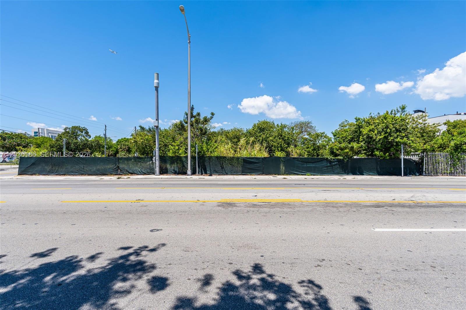 A vacant lot is enclosed by a dark green privacy fence along a paved road — 1800 NW 7th Ave, Miami FL 33136, MIAMI, FL