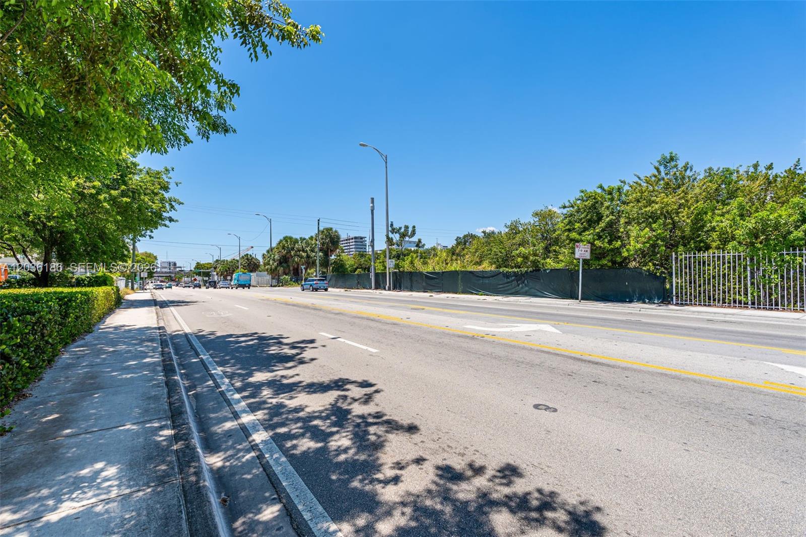 A paved road stretches past a sidewalk, green trees, and a fenced-in vacant lot — 1800 NW 7th Ave, Miami FL 33136, MIAMI, FL