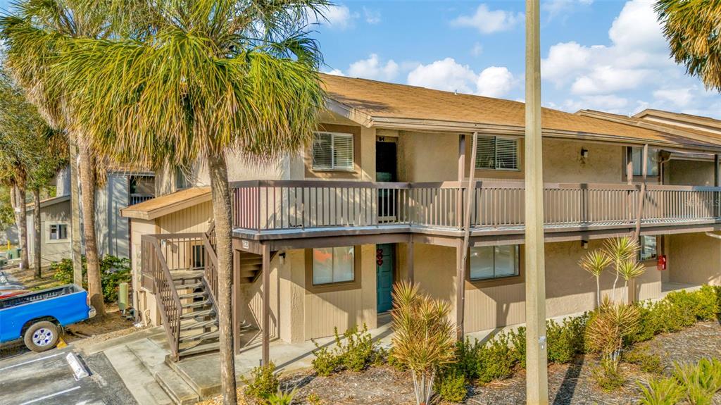 A two-story apartment building features tan stucco walls, a brown roof, and exterior wooden staircases — 6320 NEWTOWN CIRCLE UNIT 20B1, TAMPA, FL