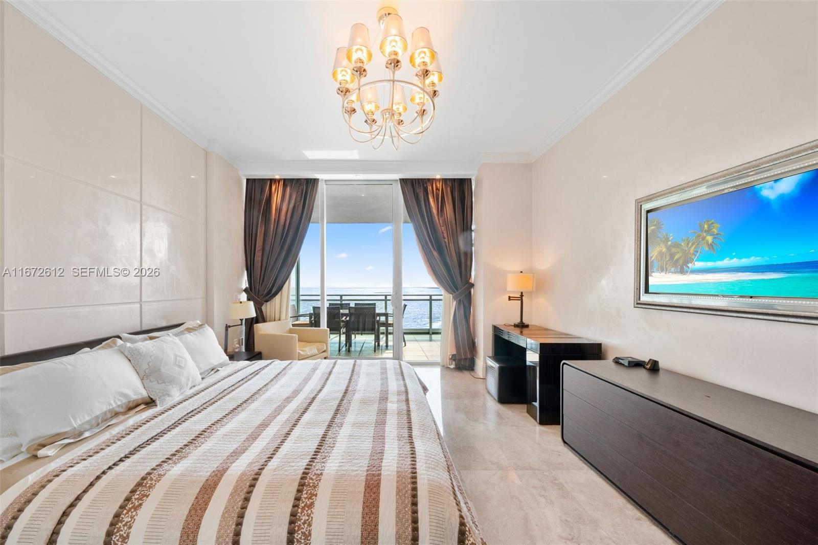 A bedroom features a striped bed, a chandelier, and a balcony overlooking the ocean — 10295 Collins Ave # 1605, Bal Harbour FL 33154, BAL HARBOUR, FL