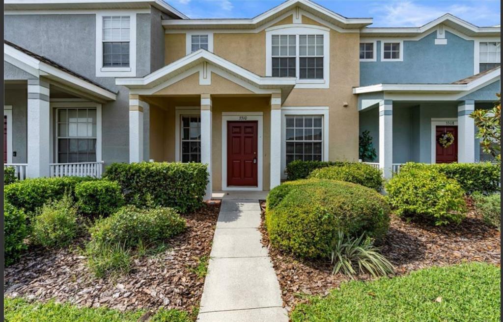 A tan two-story townhouse with a red front door and a concrete walkway — 3310 BROKEN BOW DRIVE, LAND O LAKES, FL