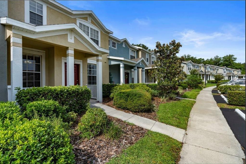 A row of two-story townhomes with covered porches, manicured landscaping, and a concrete sidewalk — 3310 BROKEN BOW DRIVE, LAND O LAKES, FL