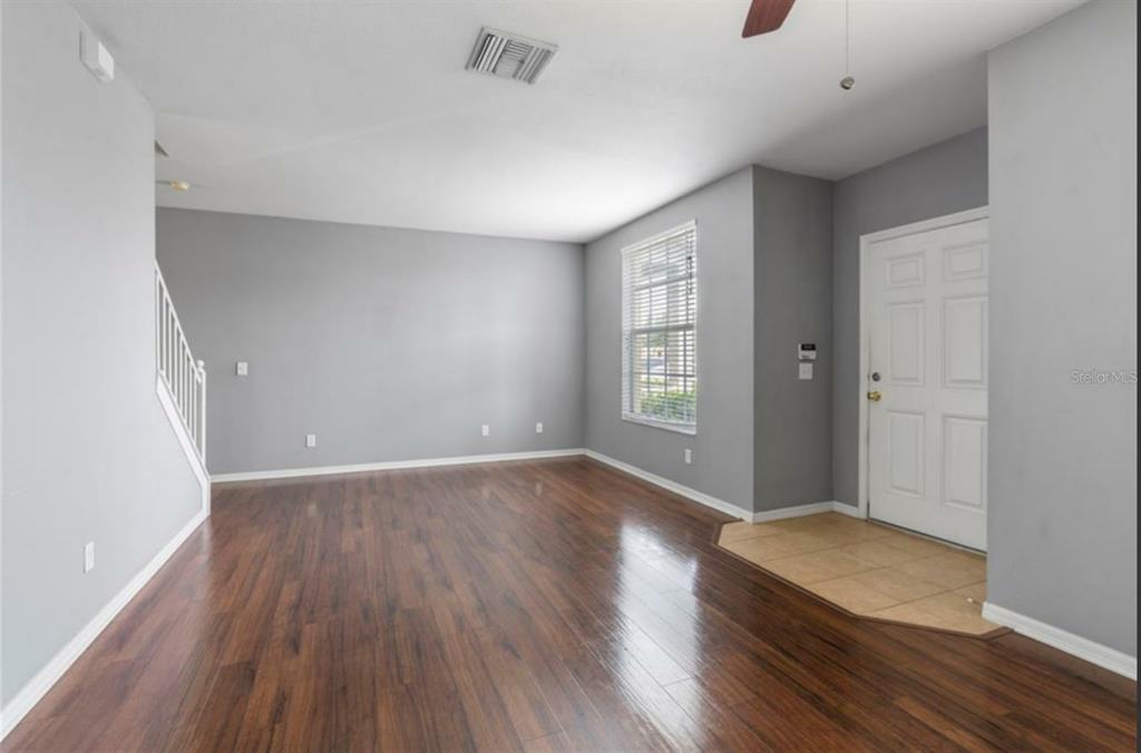 An empty living room features gray walls, dark wood-look flooring, and a tiled entryway — 3310 BROKEN BOW DRIVE, LAND O LAKES, FL