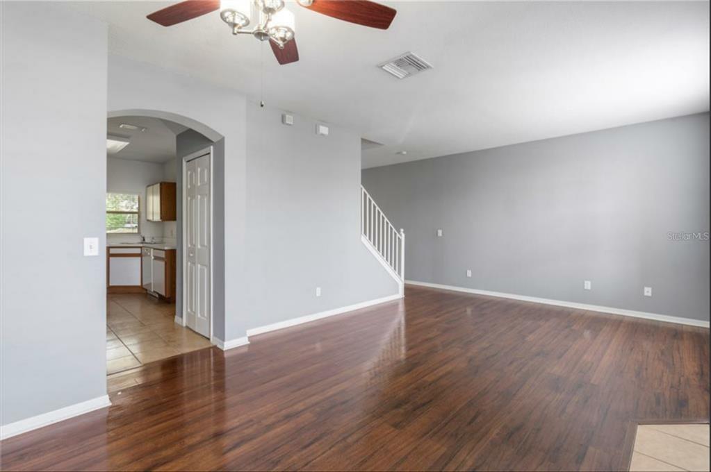 An empty living room with wood flooring, grey walls, and a staircase leading upstairs — 3310 BROKEN BOW DRIVE, LAND O LAKES, FL