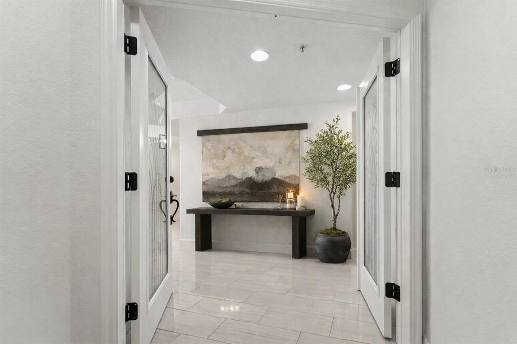 A bright entryway features white tile floors, double glass doors, and a console table with art — 1645 PINELLAS BAYWAY S UNIT B2, TIERRA VERDE, FL