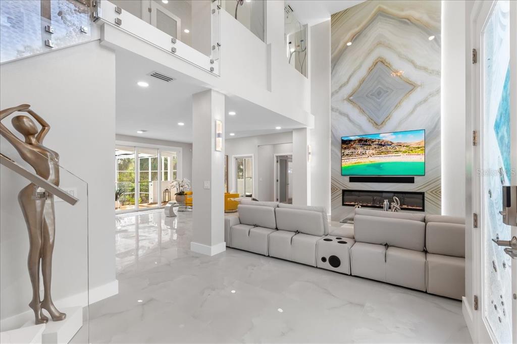 A modern living room features a tall marble accent wall, a fireplace, and white flooring — 375 WELLINGTON AVENUE, OLDSMAR, FL