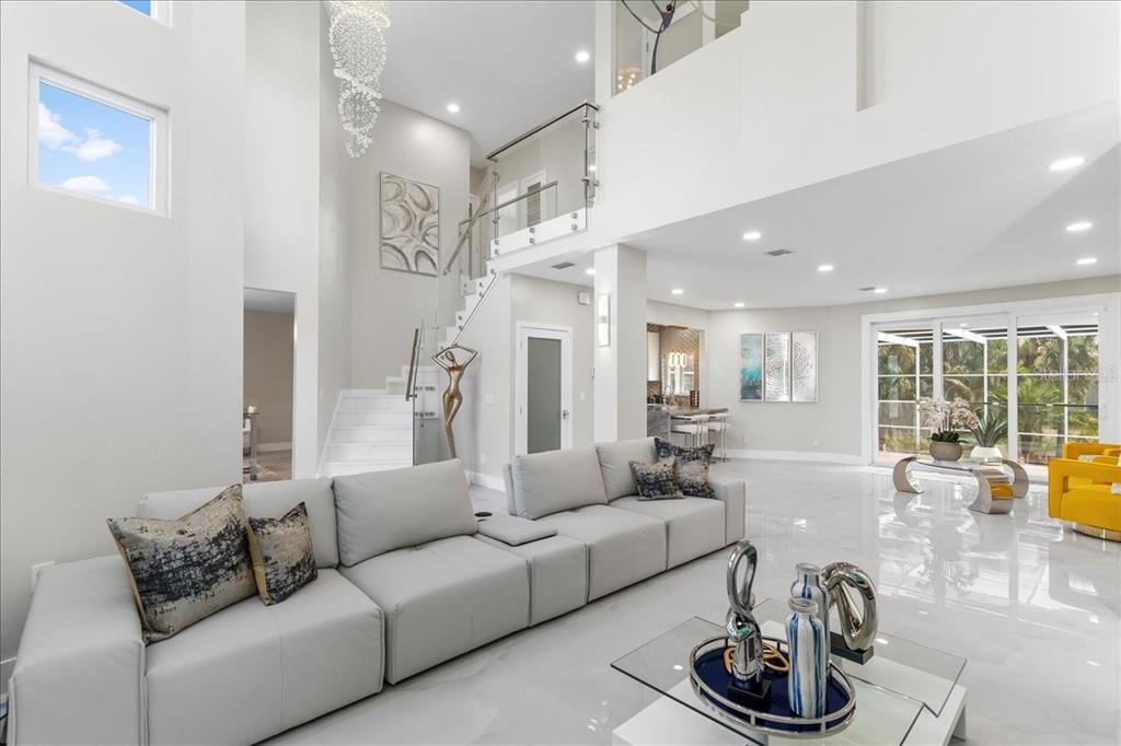 A spacious, modern living room features white tile floors, a large sectional sofa, and stairs — 375 WELLINGTON AVENUE, OLDSMAR, FL