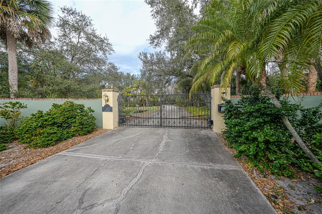 A gated concrete driveway leads to a private entrance flanked by stone pillars and landscaping — 24646 TANGERINE AVENUE, PORT CHARLOTTE, FL