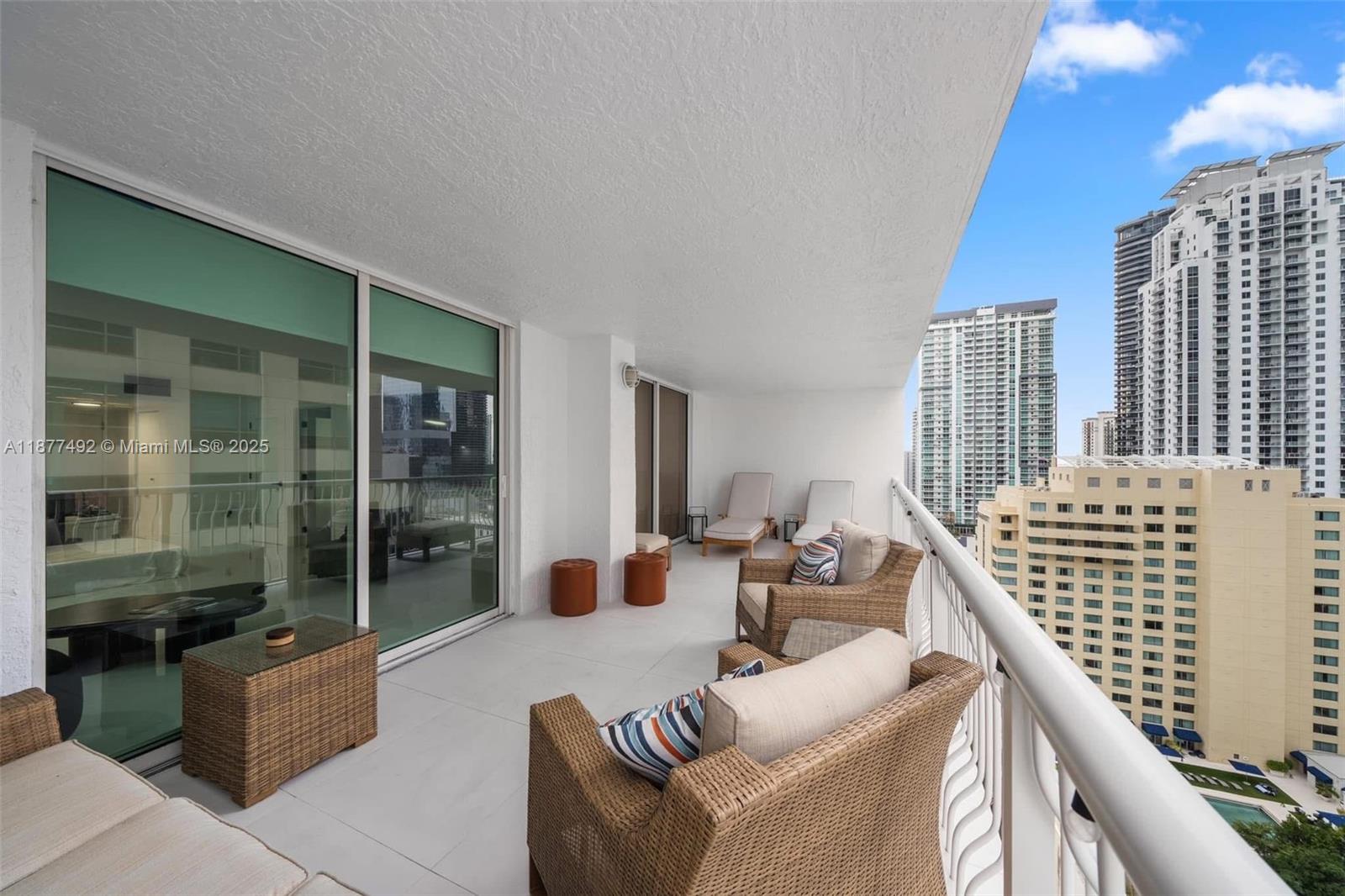 A balcony with wicker furniture overlooks a city skyline with tall residential buildings — 1200 Brickell Bay Dr # 2812, Miami FL 33131, MIAMI, FL