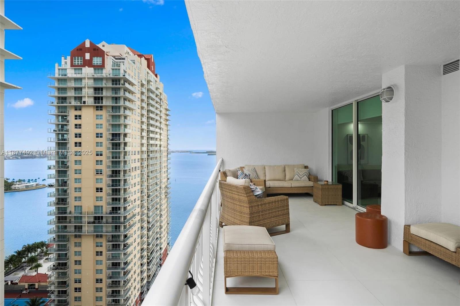 A high-rise balcony features wicker furniture and overlooks a large body of water — 1200 Brickell Bay Dr # 2812, Miami FL 33131, MIAMI, FL