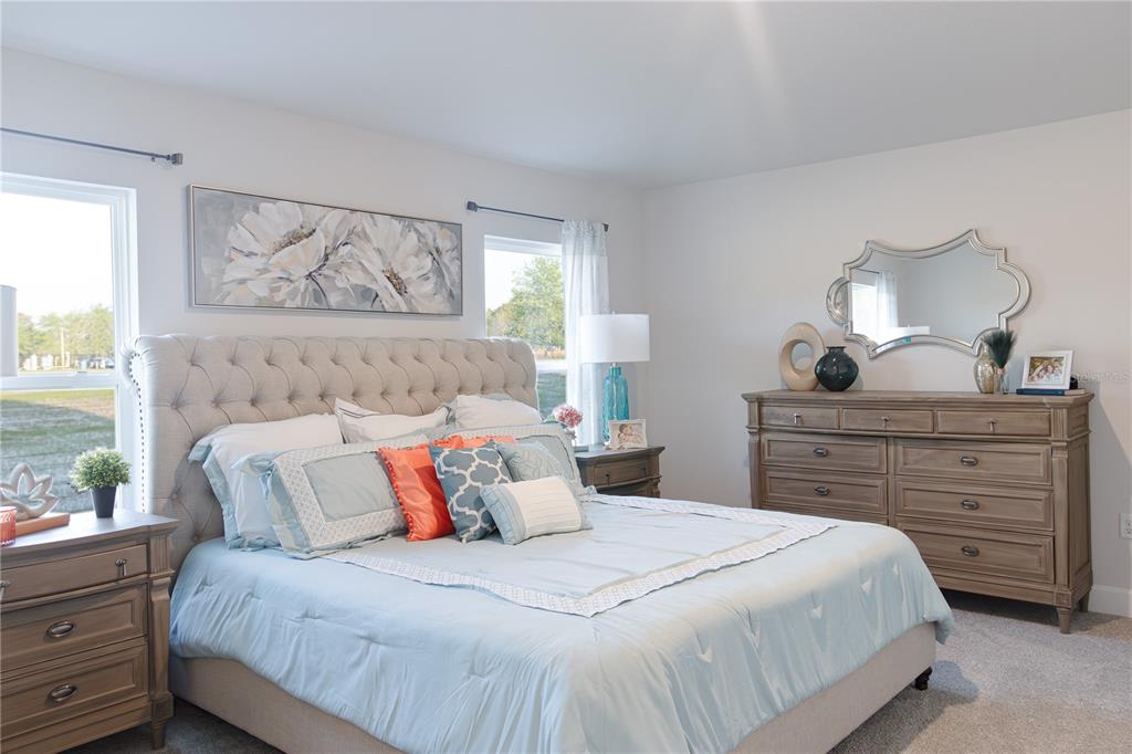 A bedroom features a tufted headboard, light blue bedding, wooden furniture, and two windows — 3312 NE CAITLIN LANE, BELL, FL