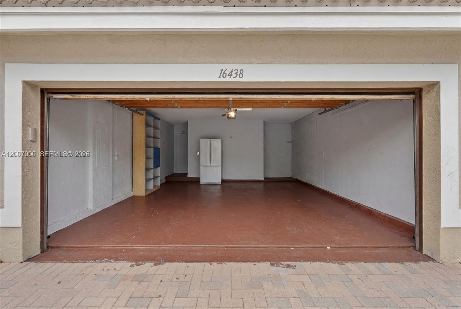 An empty garage features a painted concrete floor, a storage shelf, and a white refrigerator — 16438 SW 28th St, Miramar FL 33027, MIRAMAR, FL