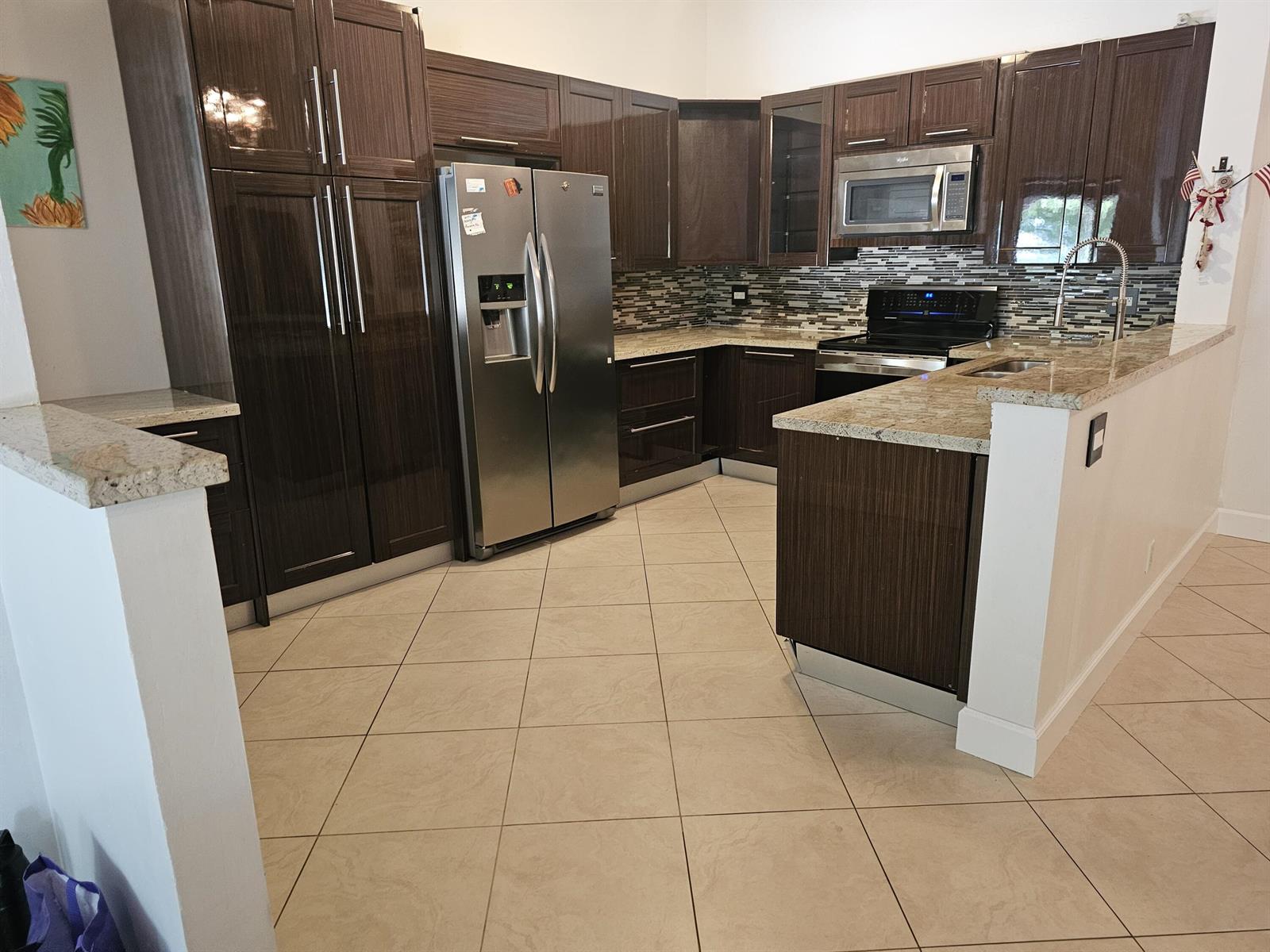 A kitchen features dark wood cabinets, stainless steel appliances, and granite countertops over tile floors — 13851 Oneida Drive # D2, Delray Beach FL 33446, DELRAY BEACH, FL