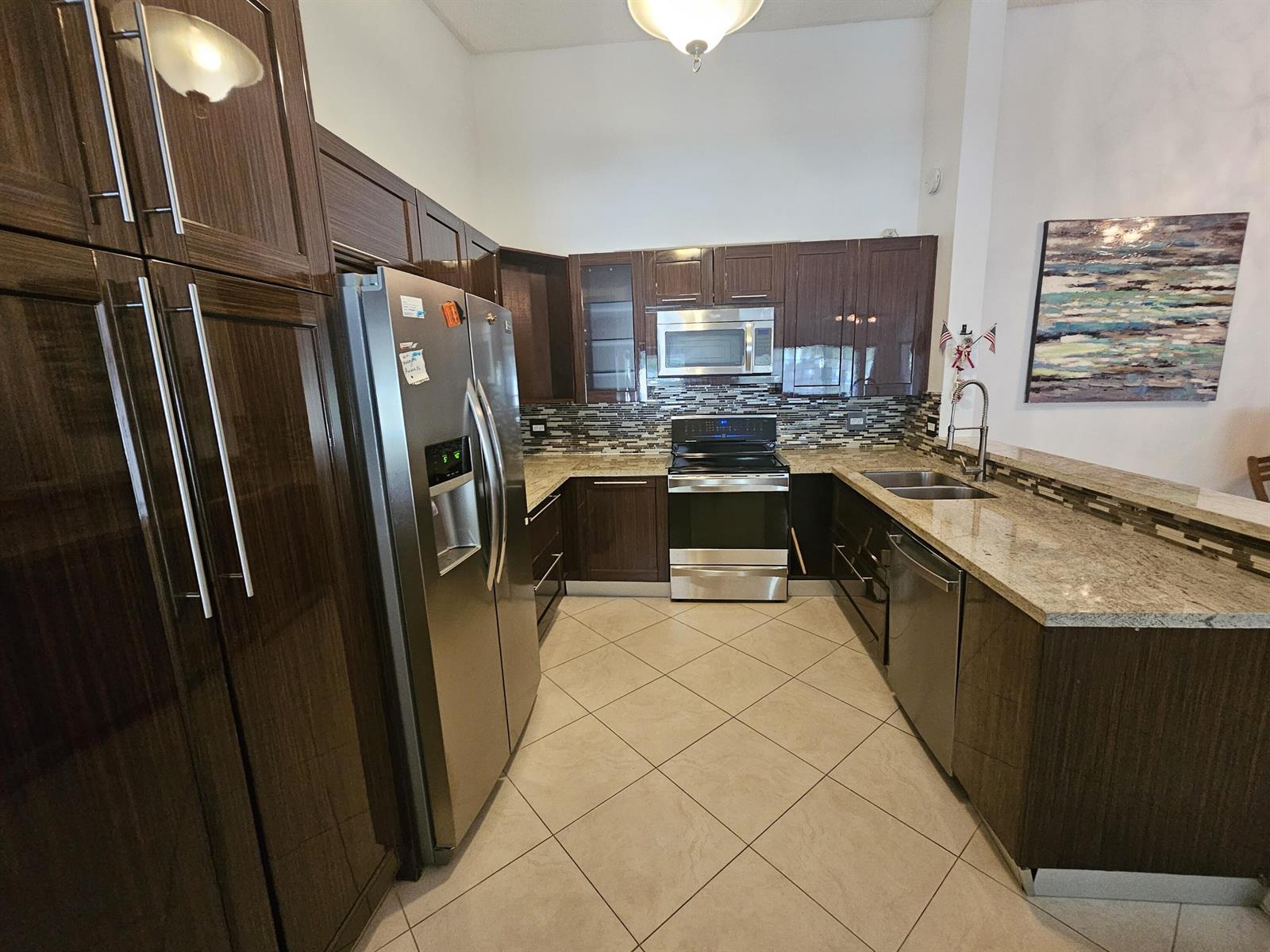 A kitchen features dark wood cabinets, stainless steel appliances, granite countertops, and tiled floors — 13851 Oneida Drive # D2, Delray Beach FL 33446, DELRAY BEACH, FL
