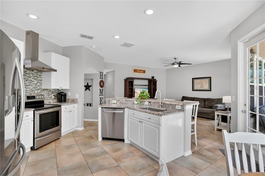 A kitchen with white cabinets, granite countertops, and stainless steel appliances opens to a living area — 2675 RUNNING SPRINGS LOOP, OVIEDO, FL
