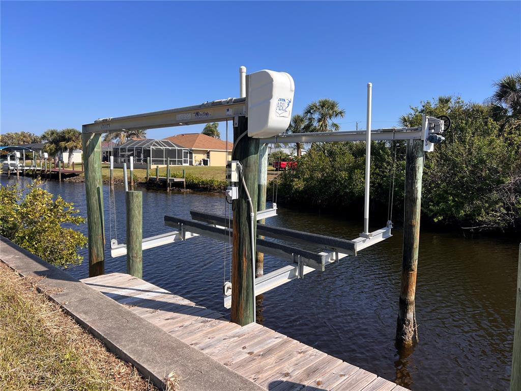 A boat lift stands over a canal next to a wooden dock and grassy bank — 4466 BAYVIEW STREET, PORT CHARLOTTE, FL