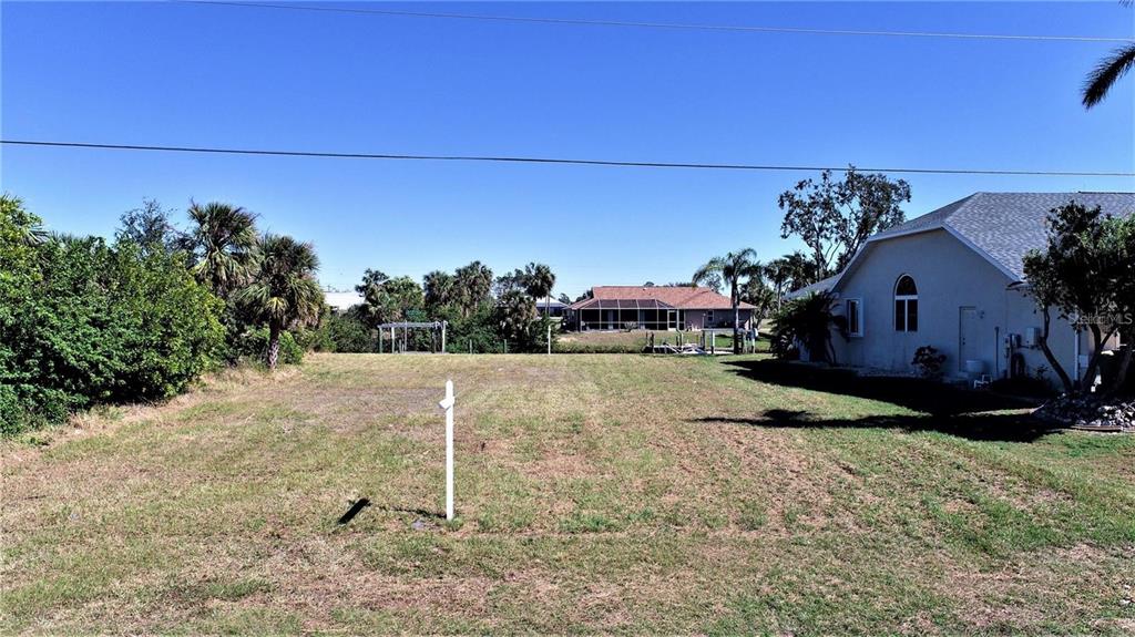 A vacant grassy lot sits between a residential house and dense trees under a clear sky — 4466 BAYVIEW STREET, PORT CHARLOTTE, FL