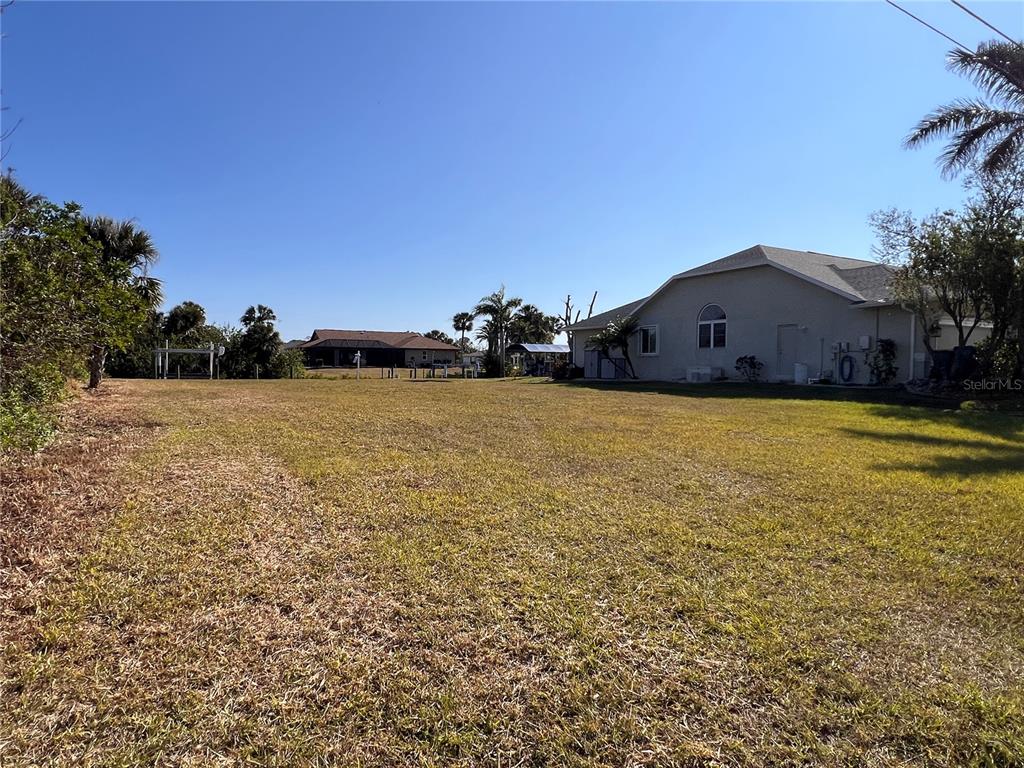 A large, grassy backyard extends toward a neighboring house under a clear blue sky — 4466 BAYVIEW STREET, PORT CHARLOTTE, FL