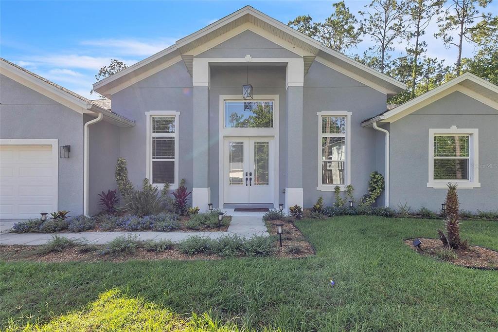 A gray single-story house features a white-trimmed double front door and a covered entryway — 17 ZEPHYR LILY PLACE, PALM COAST, FL