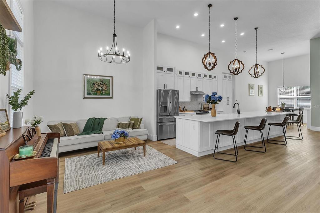 A bright open-concept living room and kitchen featuring white cabinetry, wood flooring, and pendant lighting — 17 ZEPHYR LILY PLACE, PALM COAST, FL