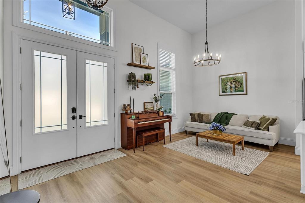 A bright entryway features a piano, a sofa, a coffee table, and a chandelier — 17 ZEPHYR LILY PLACE, PALM COAST, FL
