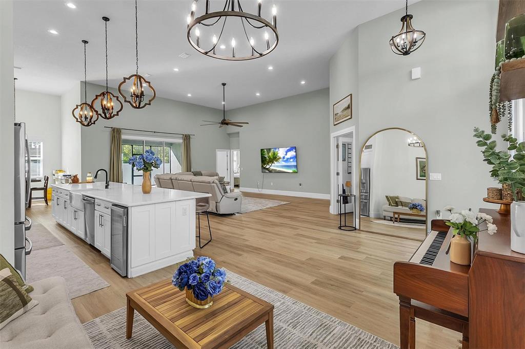 A spacious open-concept living area features a white kitchen island, wood flooring, and a piano — 17 ZEPHYR LILY PLACE, PALM COAST, FL