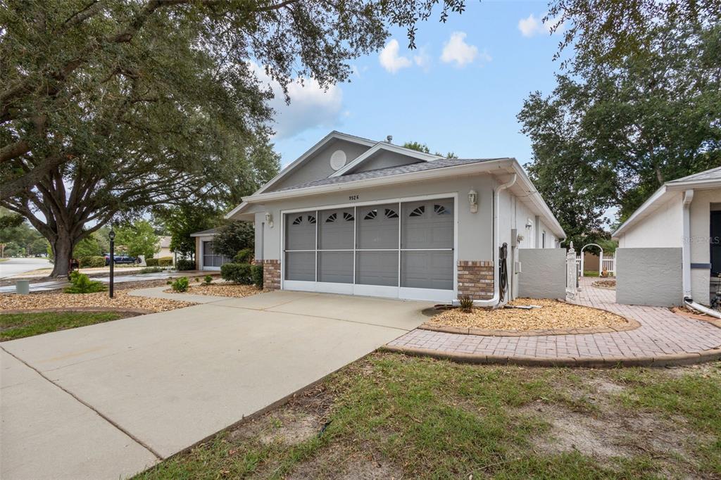 A single-story house exterior features a two-car garage with a screen door and driveway — 9526 SW 92ND PLACE ROAD, OCALA, FL