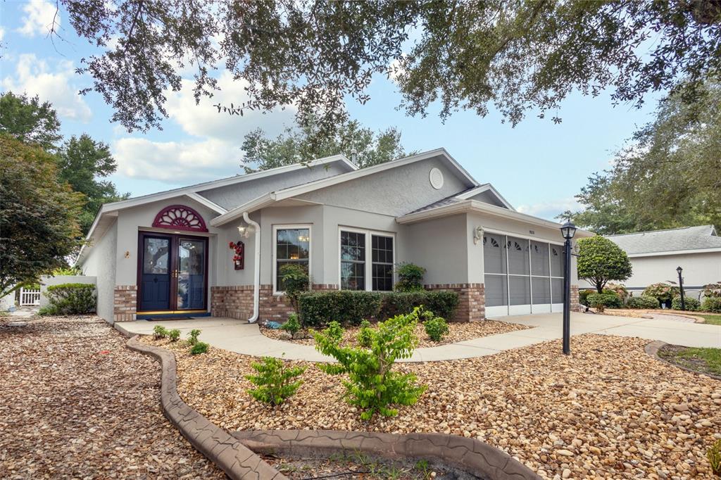 A single-story house with a gray stucco exterior, a screened garage, and a rock-covered yard — 9526 SW 92ND PLACE ROAD, OCALA, FL