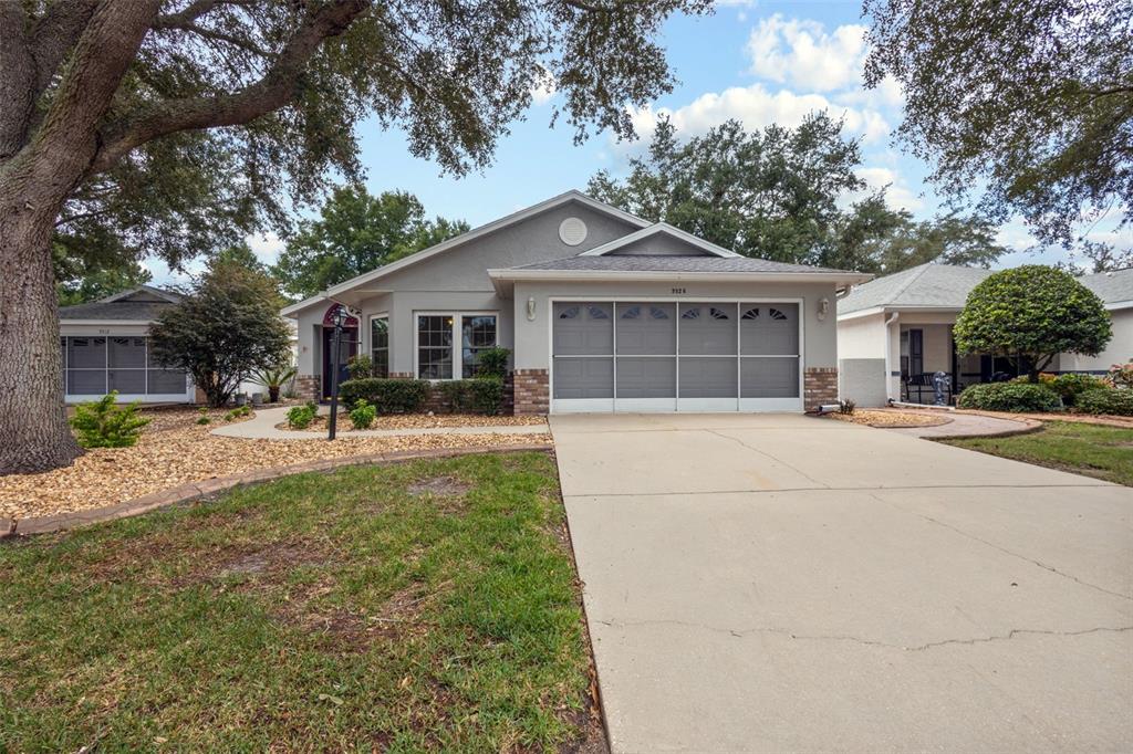 A single-story gray house with a two-car garage, a concrete driveway, and mature oak trees — 9526 SW 92ND PLACE ROAD, OCALA, FL