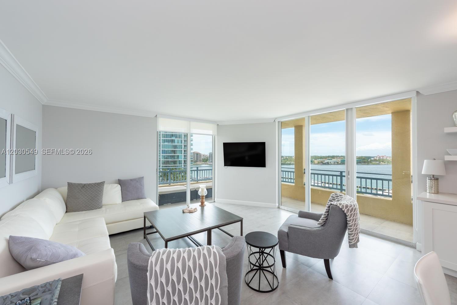 A living room with a white sectional, gray armchairs, and a balcony overlooking the water — 90 Alton Rd # 1102, Miami Beach FL 33139, MIAMI BEACH, FL