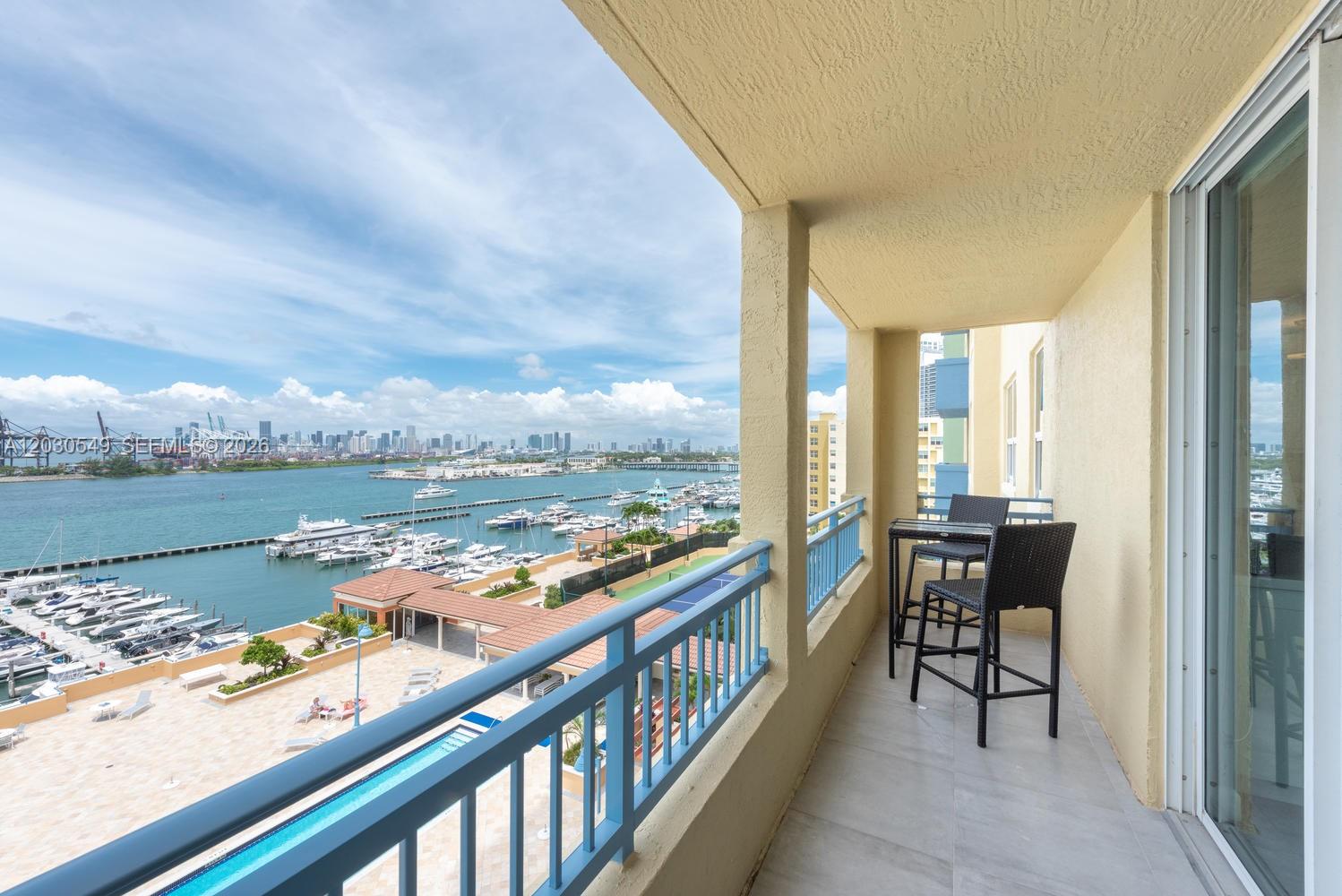 A balcony with a table and chairs overlooks a marina, swimming pool, and city skyline — 90 Alton Rd # 1102, Miami Beach FL 33139, MIAMI BEACH, FL