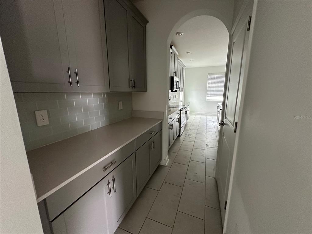 A hallway with grey cabinets and a countertop leads to a kitchen through an archway — 3115 ADDISON BOULEVARD, ST CLOUD, FL