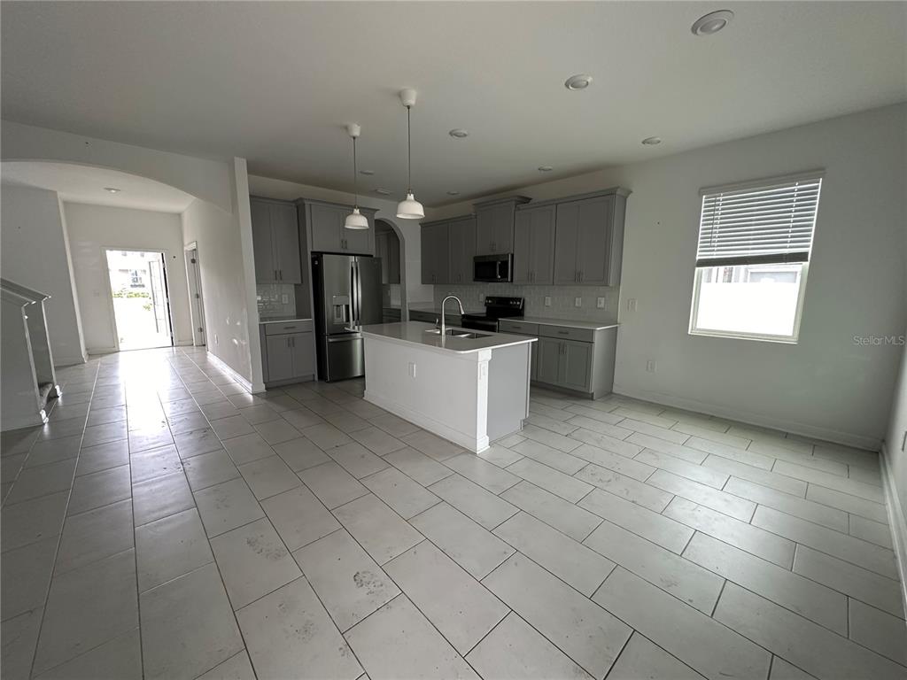 A kitchen features gray cabinetry, a white island, stainless steel appliances, and light tile flooring — 3115 ADDISON BOULEVARD, ST CLOUD, FL