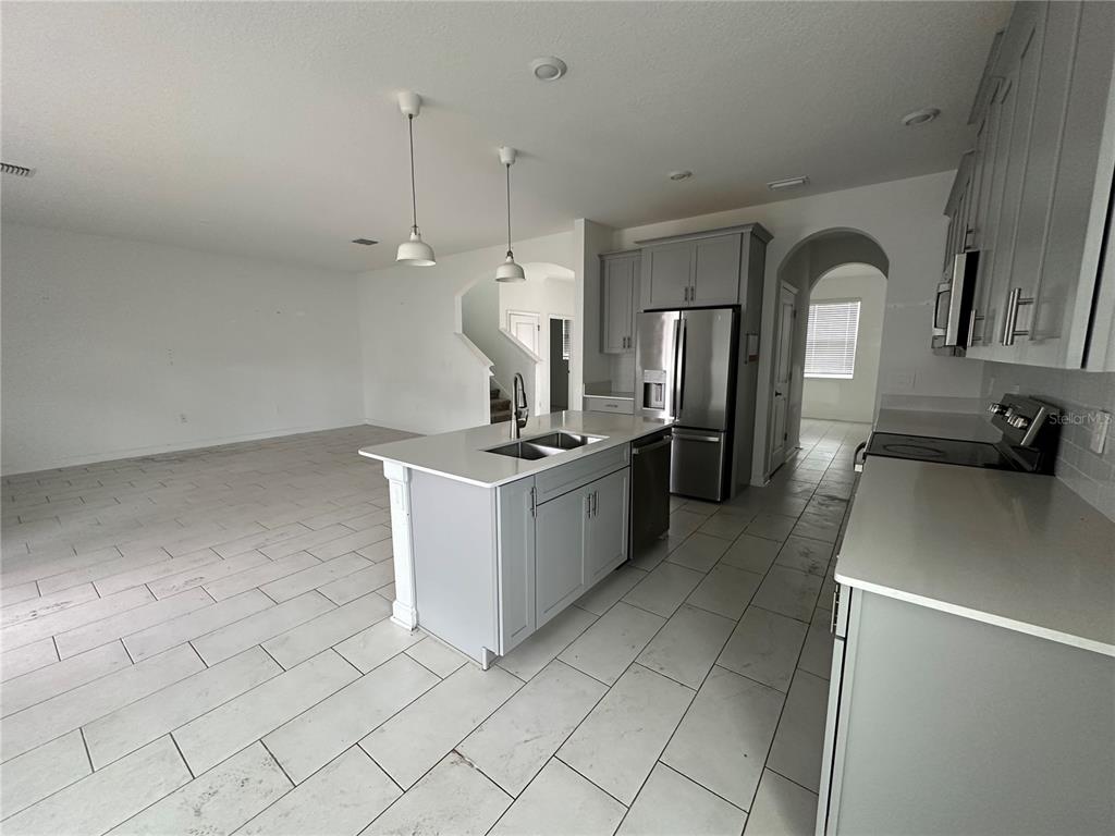 A kitchen features gray cabinets, a central island with a sink, and light-colored tile flooring — 3115 ADDISON BOULEVARD, ST CLOUD, FL