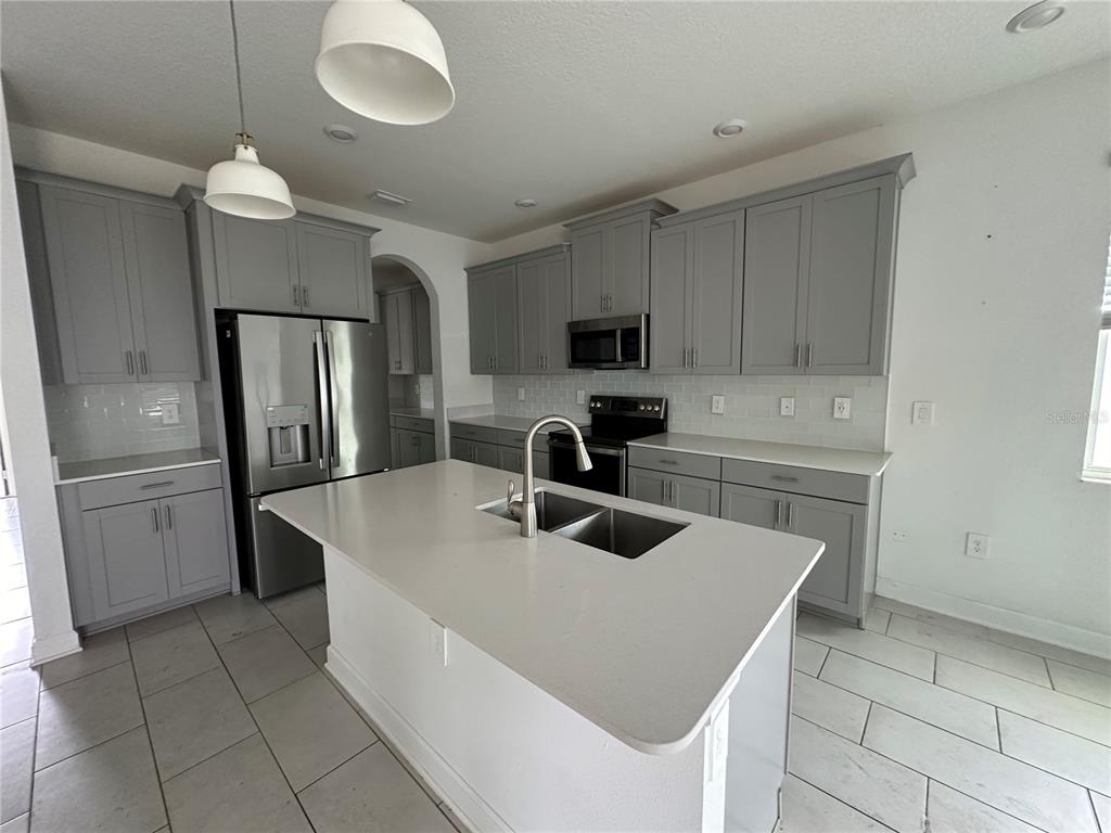 A kitchen features gray shaker cabinets, a central island with a sink, and white countertops — 3115 ADDISON BOULEVARD, ST CLOUD, FL