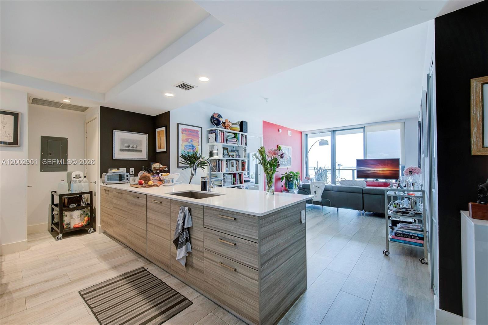 A modern kitchen with wood-grain cabinets and a white island overlooks an open living area — 121 NE 34th St # 1607, Miami FL 33137, MIAMI, FL