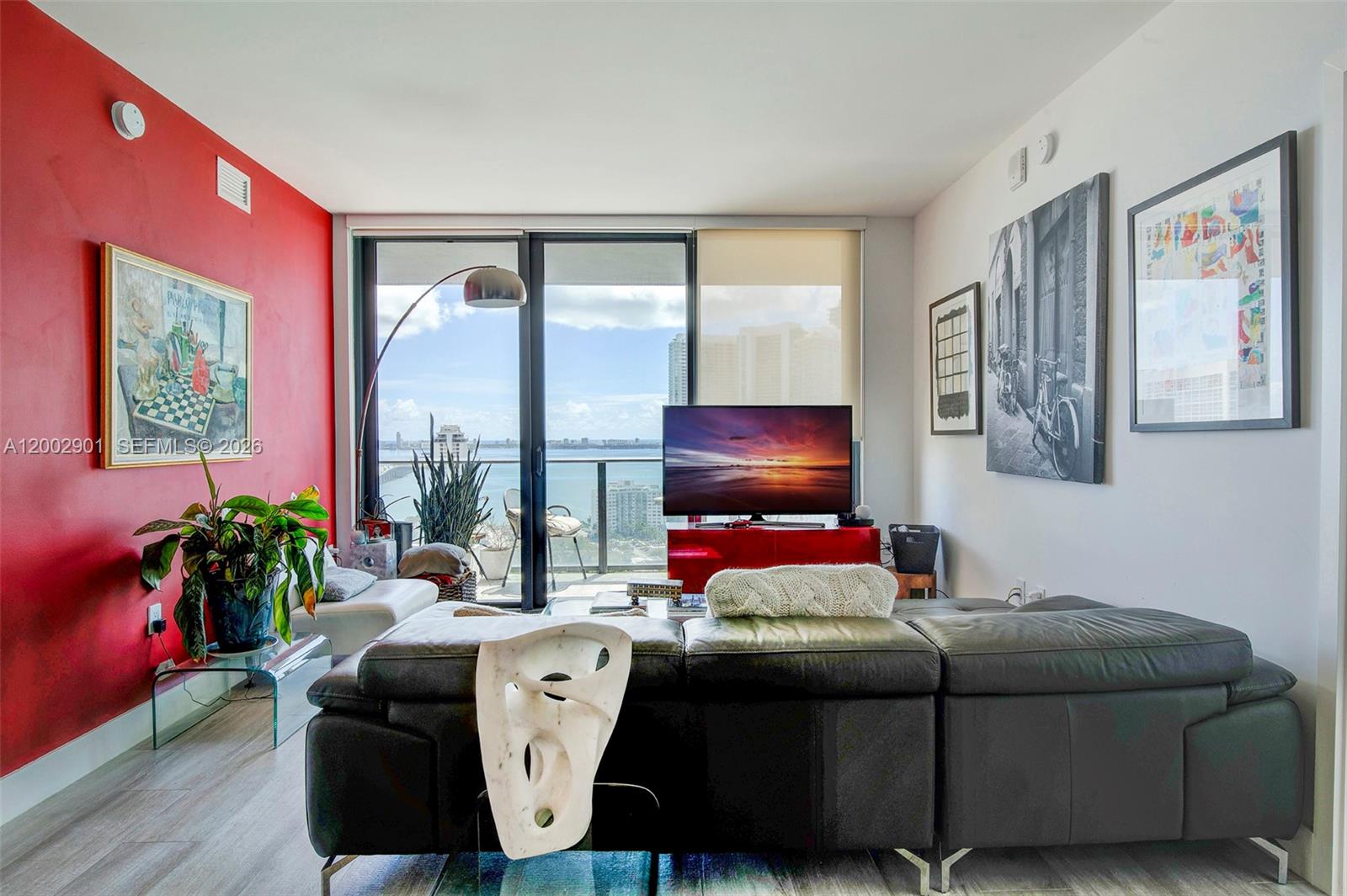 A living room features a red accent wall, a black leather sofa, and a balcony view — 121 NE 34th St # 1607, Miami FL 33137, MIAMI, FL