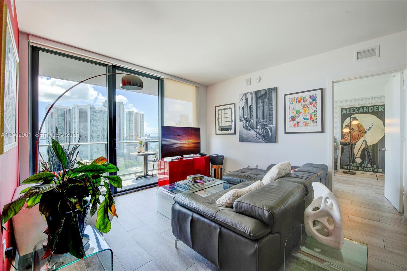 A modern living room features a grey sectional sofa, a red media console, and balcony views — 121 NE 34th St # 1607, Miami FL 33137, MIAMI, FL