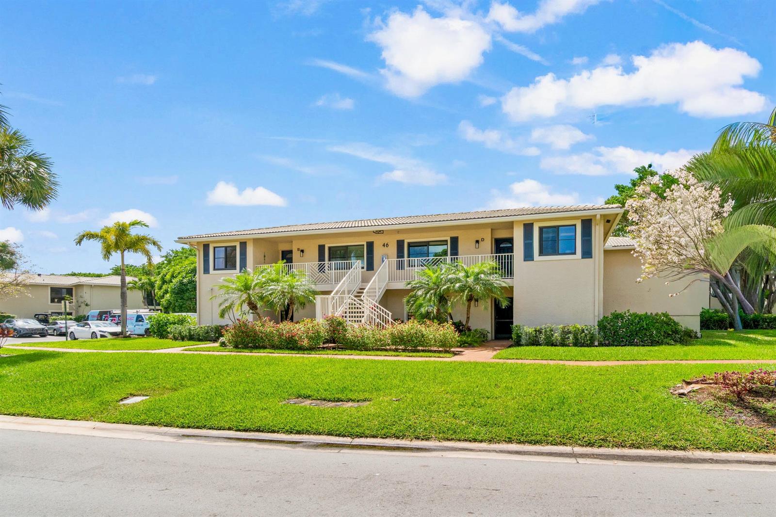 A two-story apartment building with a central staircase, beige stucco walls, and surrounding landscaping — 46 Stratford Lane W # D, Boynton Beach FL 33436, BOYNTON BEACH, FL