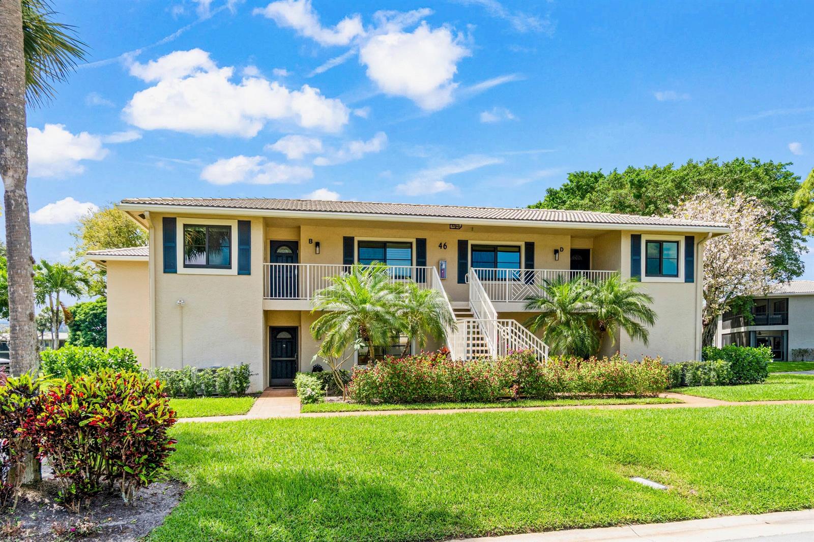 A two-story apartment building with beige stucco walls, dark shutters, and a central staircase — 46 Stratford Lane W # D, Boynton Beach FL 33436, BOYNTON BEACH, FL