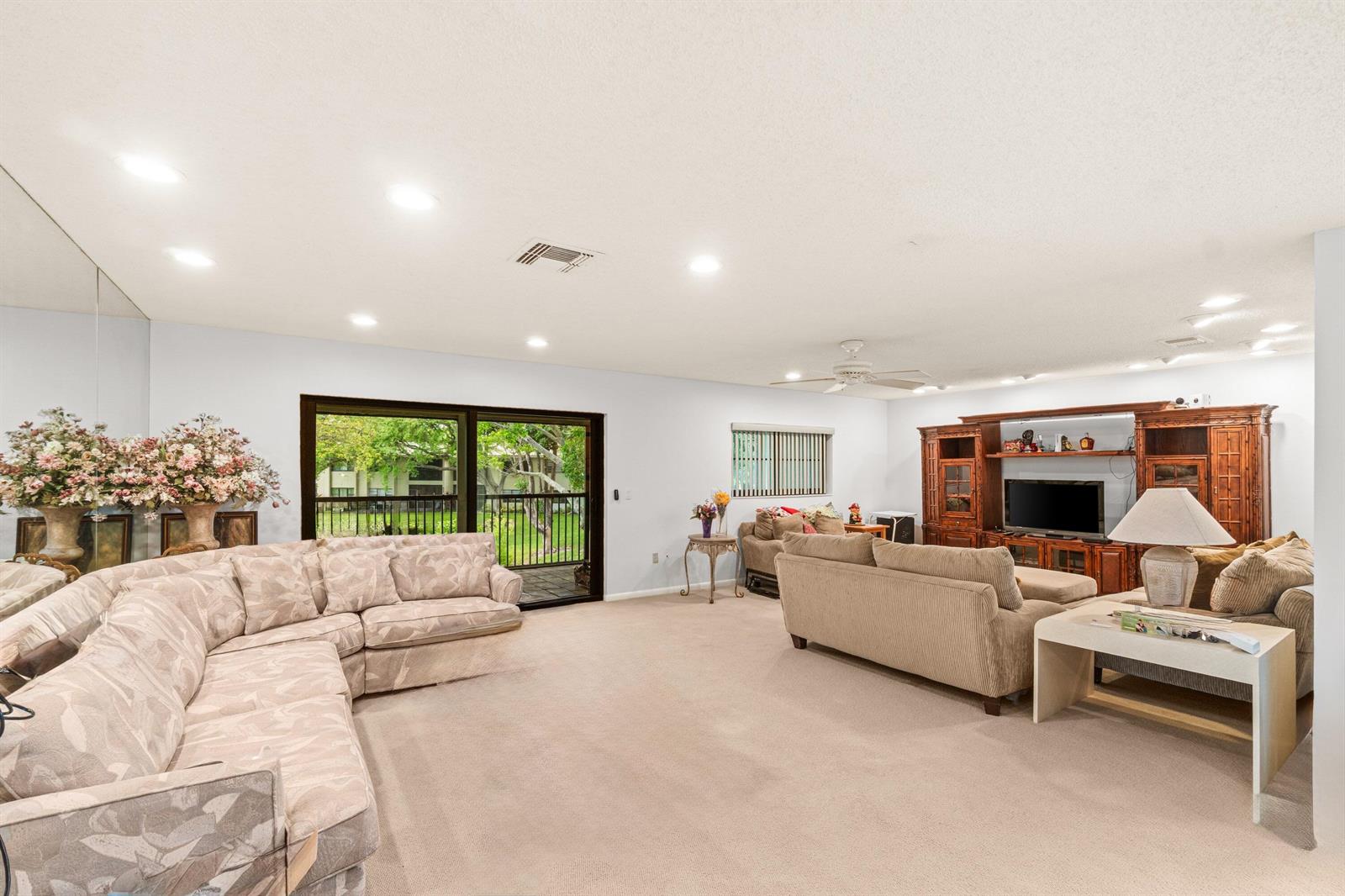 A spacious living room features beige carpeting, two large sofas, and a wooden entertainment center — 46 Stratford Lane W # D, Boynton Beach FL 33436, BOYNTON BEACH, FL
