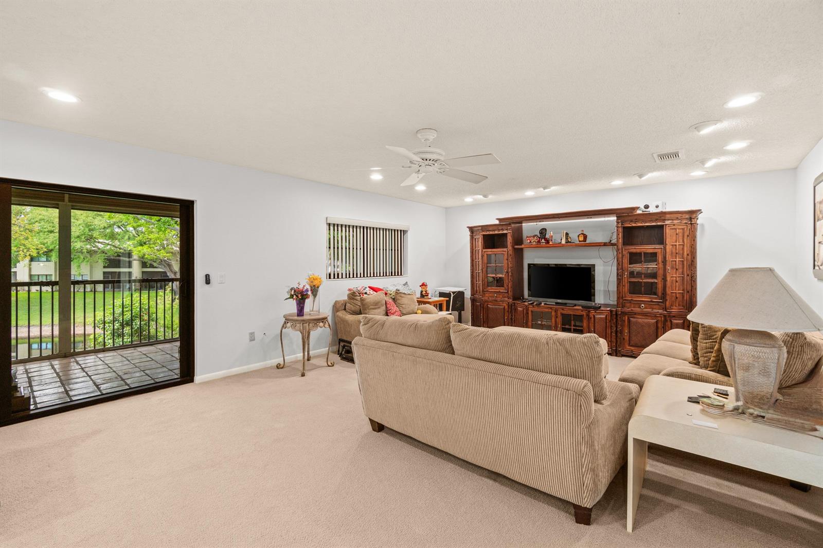 A living room features beige carpet, a large wooden entertainment center, and a sliding glass door — 46 Stratford Lane W # D, Boynton Beach FL 33436, BOYNTON BEACH, FL