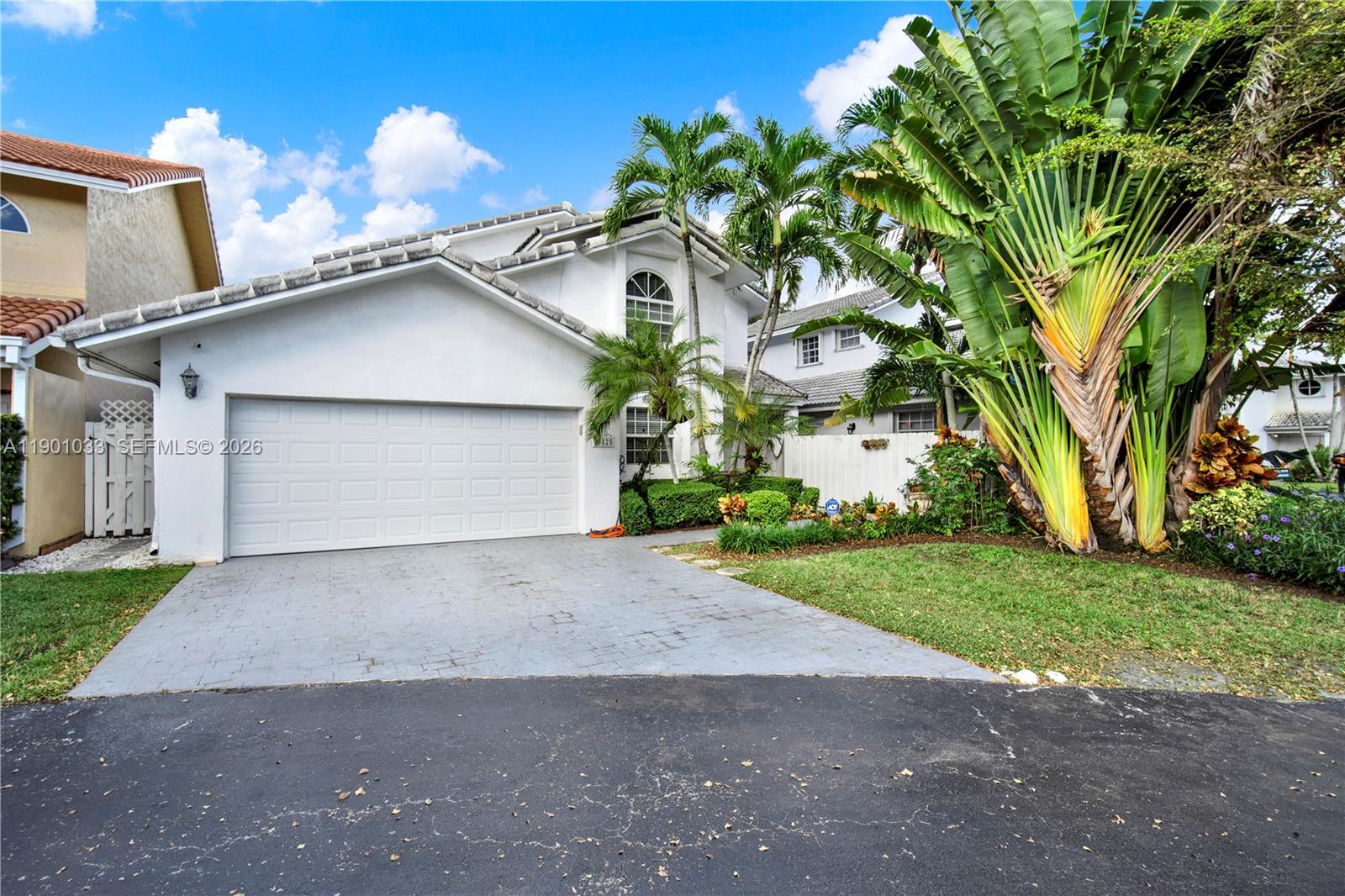 A two-story white house features a two-car garage, a paved driveway, and lush tropical landscaping — 10825 SW 91st Ln, Miami FL 33176, MIAMI, FL