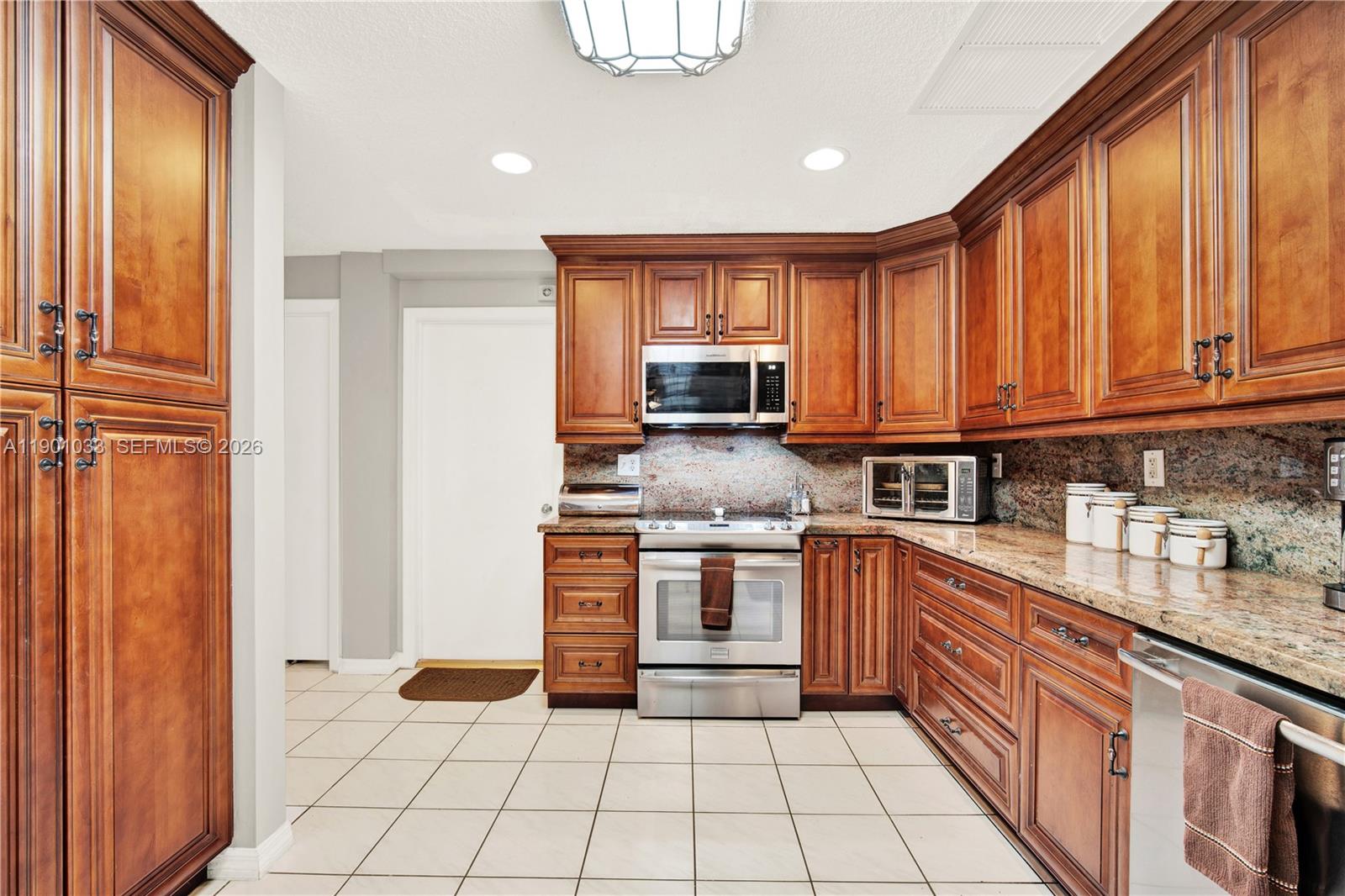 A kitchen features wood cabinets, granite countertops, stainless steel appliances, and light-colored tile flooring — 10825 SW 91st Ln, Miami FL 33176, MIAMI, FL