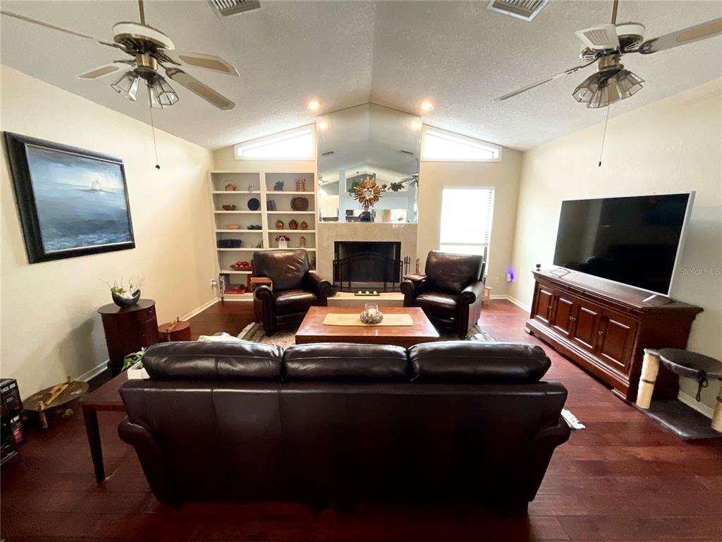 A living room features dark leather furniture, a fireplace, built-in shelves, and wood flooring — 1349 HILLSIDE DRIVE, TARPON SPRINGS, FL