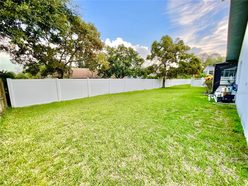 A grassy backyard features a white vinyl fence and mature trees under a cloudy sky — 1349 HILLSIDE DRIVE, TARPON SPRINGS, FL