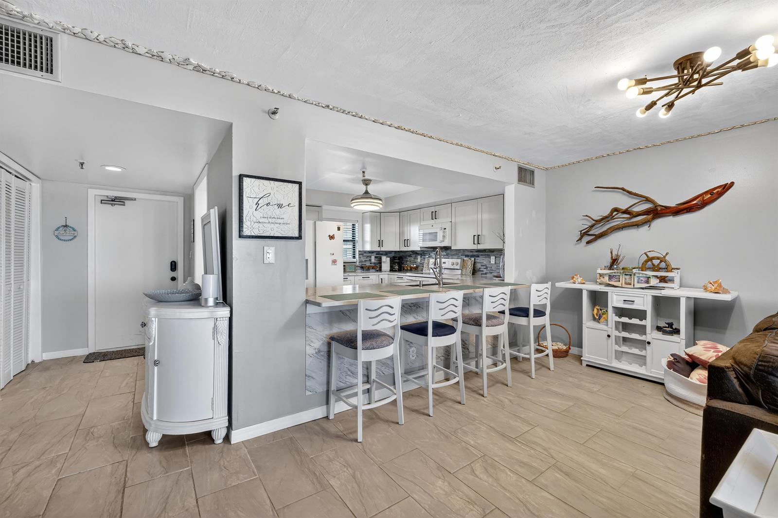 A kitchen with white cabinets and a breakfast bar overlooks a tiled living area — 801 S Ocean Drive # 910, Fort Pierce FL 34949, FORT PIERCE, FL