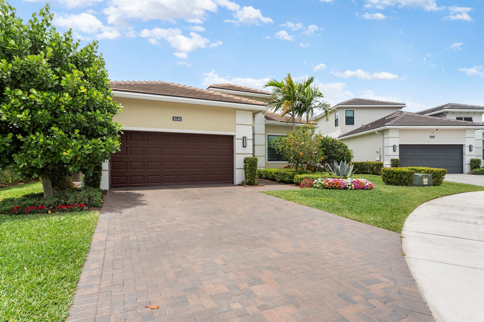 A beige house with a brown garage door and a brick driveway under a blue sky — 16148 Key Biscayne Lane, Westlake FL 33470, WESTLAKE, FL