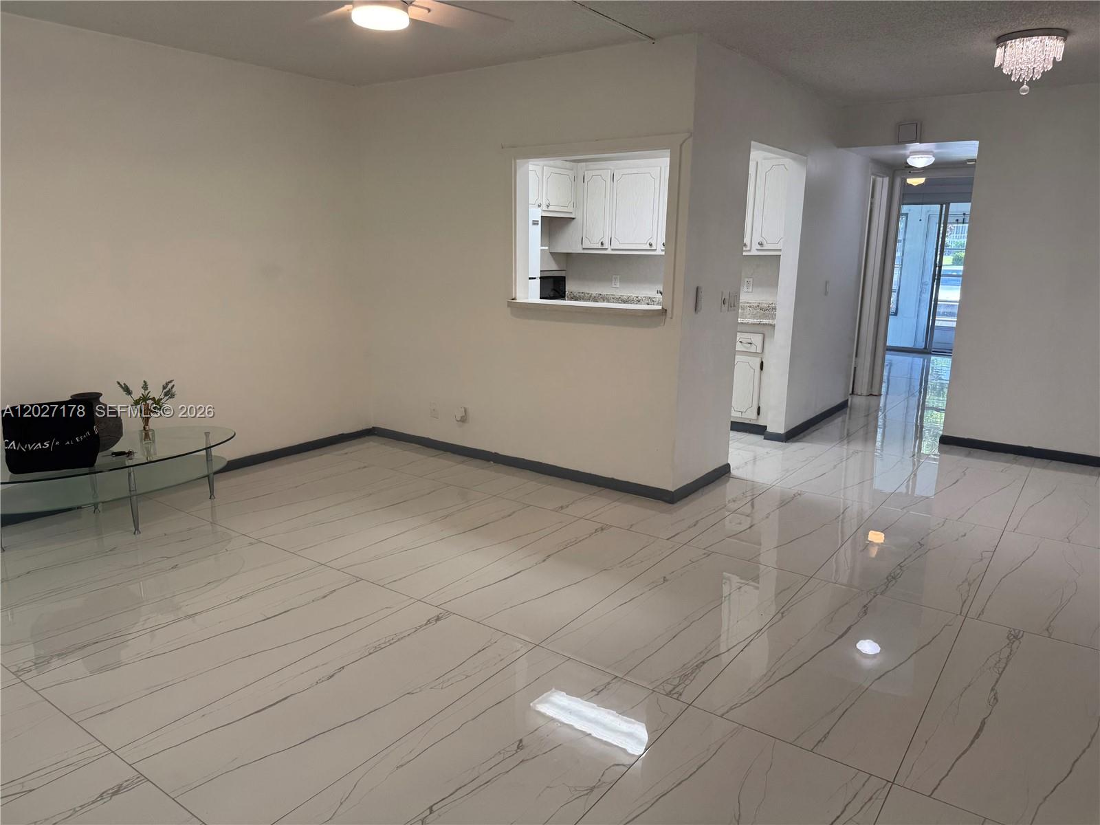 A bright living area features white marble-look tile flooring and a kitchen pass-through window — 111 Tilford F # 111, Deerfield Beach FL 33442, DEERFIELD BEACH, FL