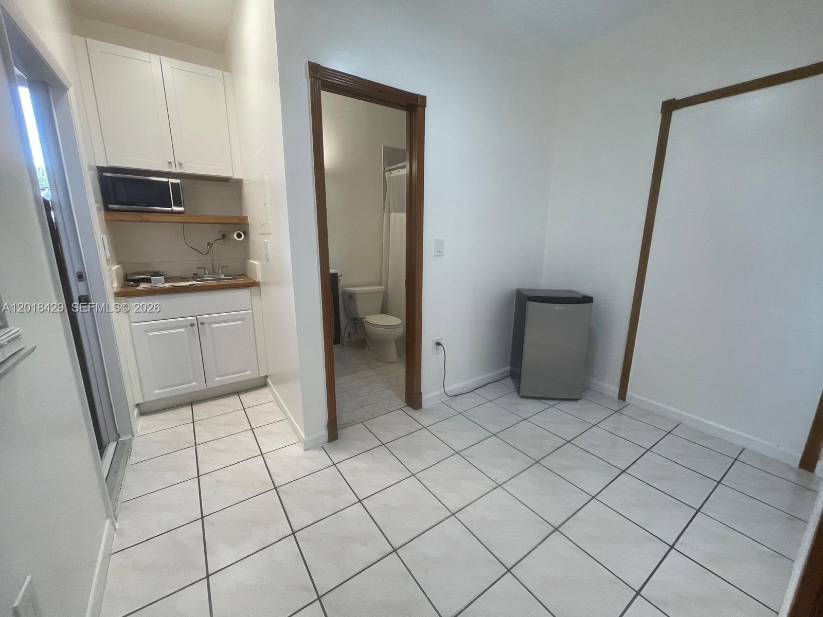 A small kitchen area with white cabinets and a bathroom doorway on tiled floors — 3531 SW 13th St # A, Miami FL 33145, MIAMI, FL